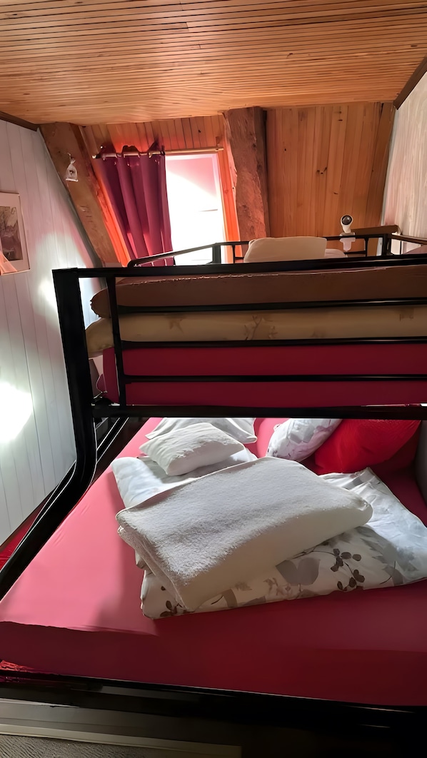 A bunk bed with a red mattress and white pillows, wooden walls, and a window with curtains.