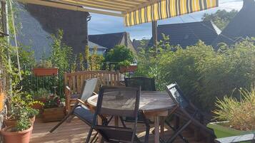 An outdoor patio with a wooden table and chairs, surrounded by potted plants and a pergola.