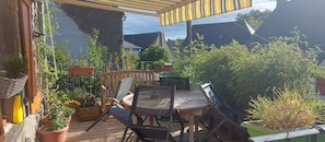 An outdoor patio with a wooden table and chairs, surrounded by potted plants and a pergola.