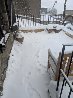 A snow-covered outdoor area with a wooden bench, a potted plant, and a metal fence.