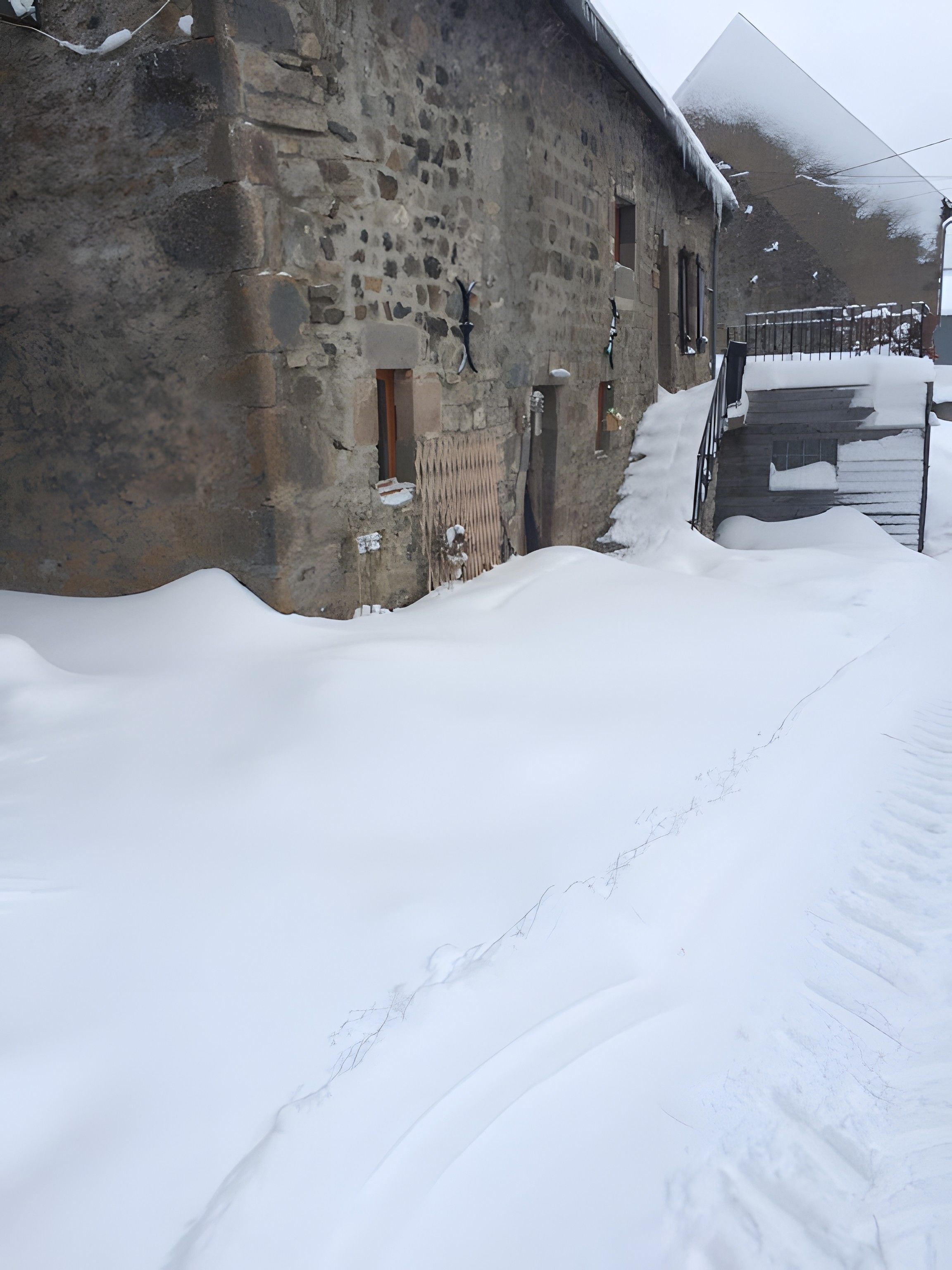 Een stenen gebouw met een met sneeuw bedekte grond, een houten deur en een metalen poort.