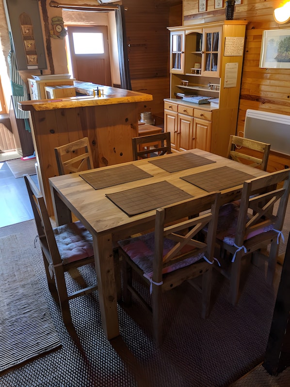 A wooden interior with a dining table, chairs, a kitchen area, and a window.