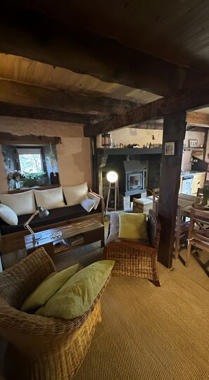 A cozy living room with a sofa, a wicker chair, a wooden table, and a stone fireplace.