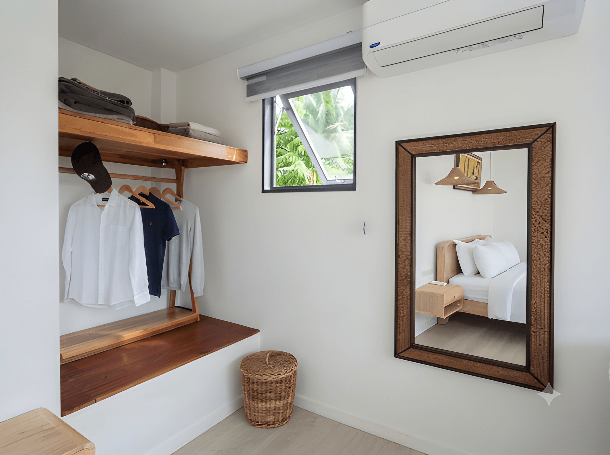 A compact hotel room with a wooden bench, a mirror, a small window, and a wall-mounted air conditioner.