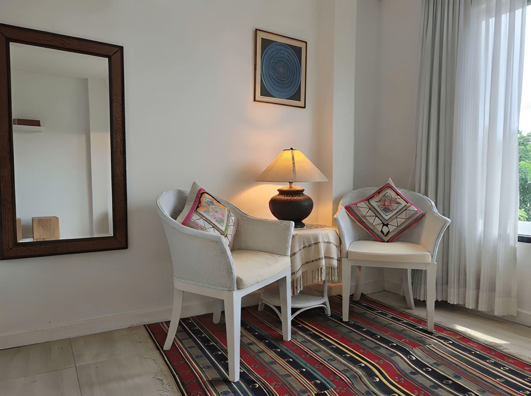 Een kamer met twee witte stoelen, een tafel met een lamp, een spiegel en een kamerbreed tapijt met dessin.