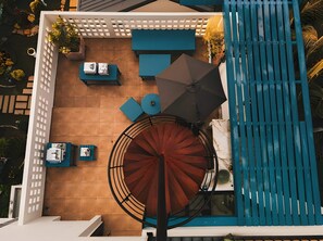 Un espacio exterior con asientos, una escalera en espiral, una piscina y una pérgola blanca.