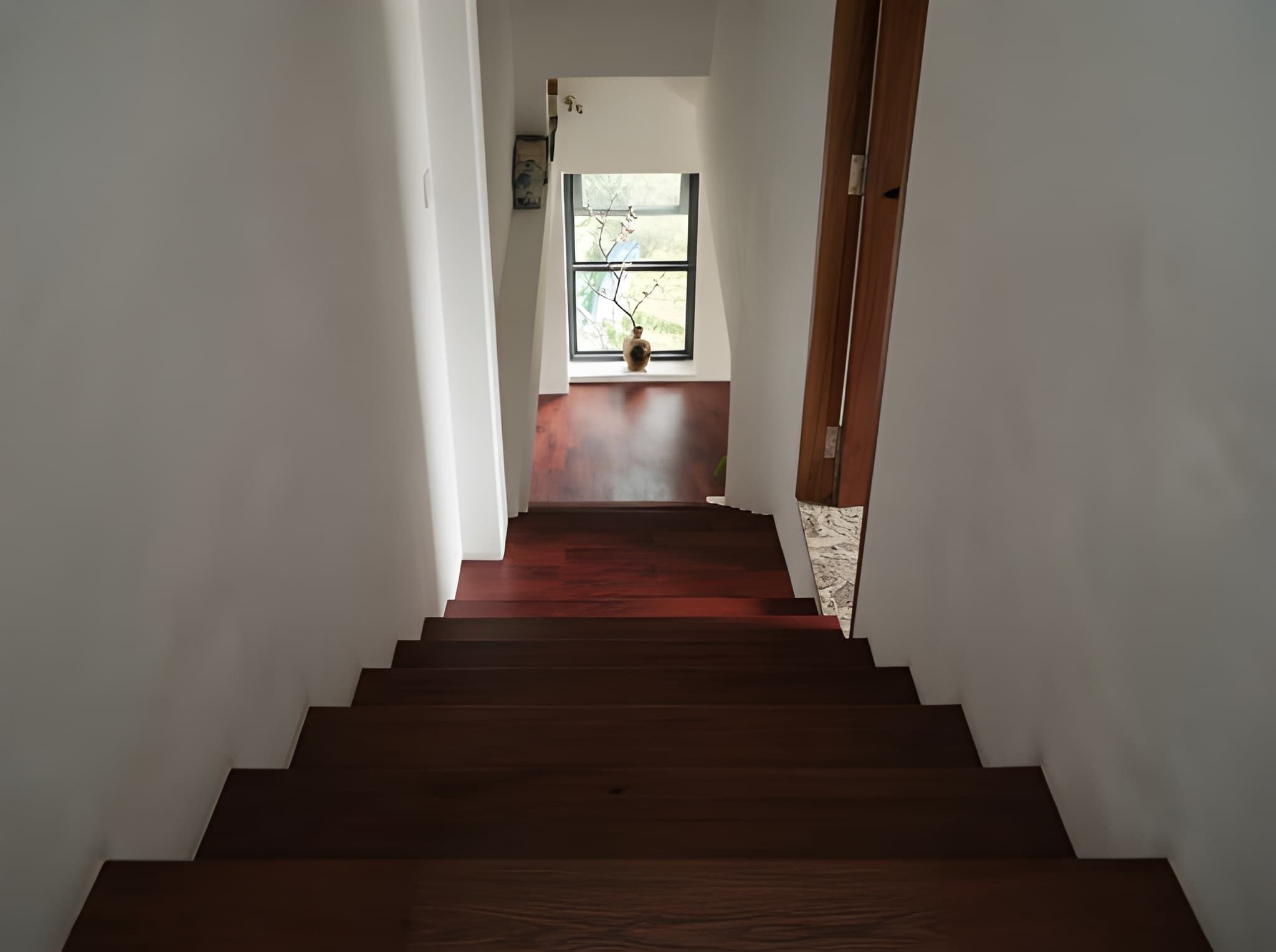 A wooden staircase leading to a room with a window and a vase on the sill.