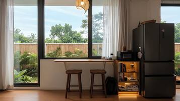 A modern kitchen with a large window, wooden stools, a black refrigerator, and a hanging light fixture.