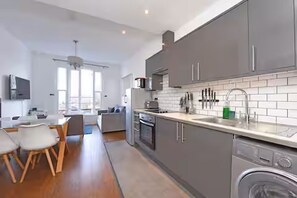A modern kitchen with grey cabinets, a dishwasher, and a dining area with a table and chairs. - Bright 3BR Next to Clapham Junction | 1m to Trains (London)