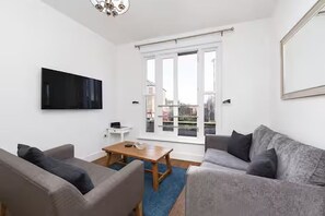 A modern living room with a flat-screen TV, a wooden coffee table, and two sofas. - Bright 3BR Next to Clapham Junction | 1m to Trains (London)