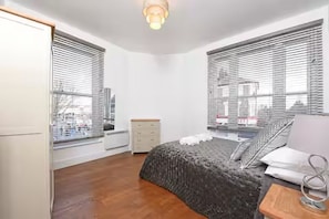 A bedroom with a bed, bedside table, dresser, and windows with blinds. - Bright 3BR Next to Clapham Junction | 1m to Trains (London)