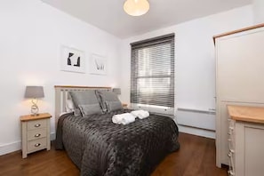 A bedroom with a bed, bedside table, lamp, and a window with blinds. - Bright 3BR Next to Clapham Junction | 1m to Trains (London)