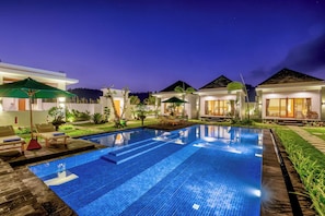 A swimming pool with lounge chairs and umbrellas, surrounded by modern houses with large windows and a clear night sky. - Green Onion Villa – Your Cozy Stay Near Mount Batur (Denpasar)