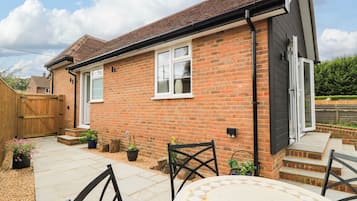 A brick house with a tiled patio, a wooden gate, and a small outdoor seating area with chairs.