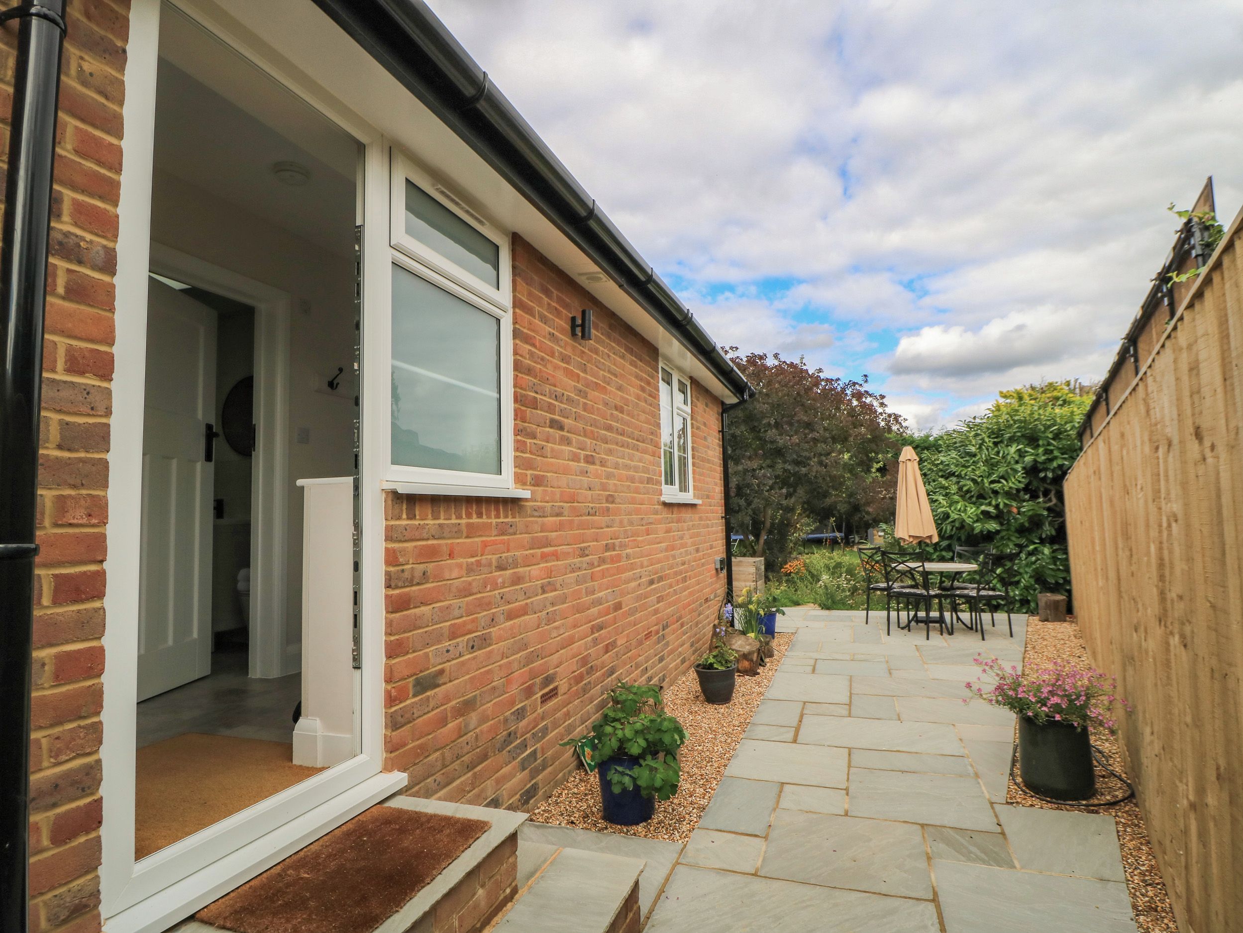 A brick house with a visible door, a window, and a garden with a patio table and chairs.