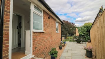 A brick house with a visible door, a window, and a garden with a patio table and chairs.