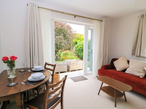 A dining area with a table set for two, a red sofa, and a view of a garden through a glass door. - Kingswick Lodge (High Wycombe)