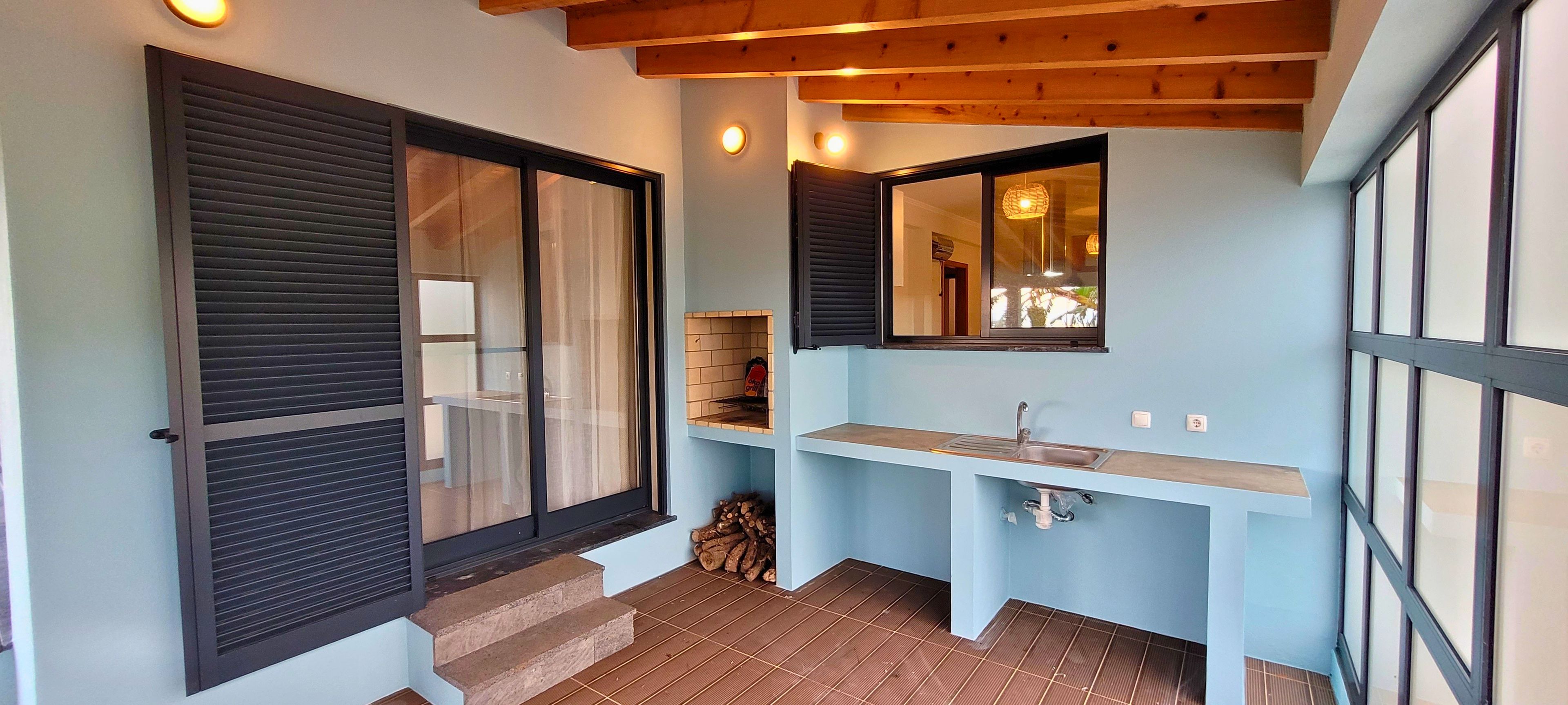 Un baño con lavamanos, espejo y ventana con contraventanas.