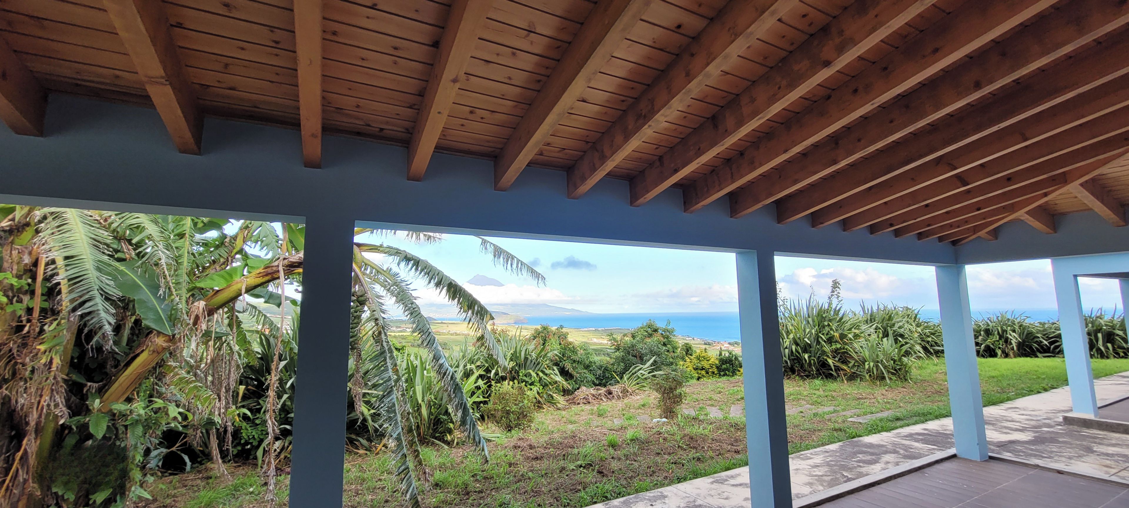 A covered outdoor area with a view of a landscape including greenery and a distant view of the sea.