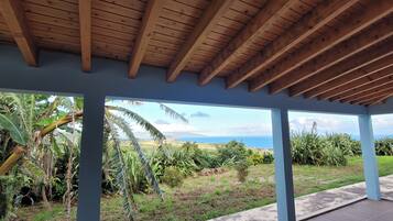A covered outdoor area with a view of a landscape including greenery and a distant view of the sea.