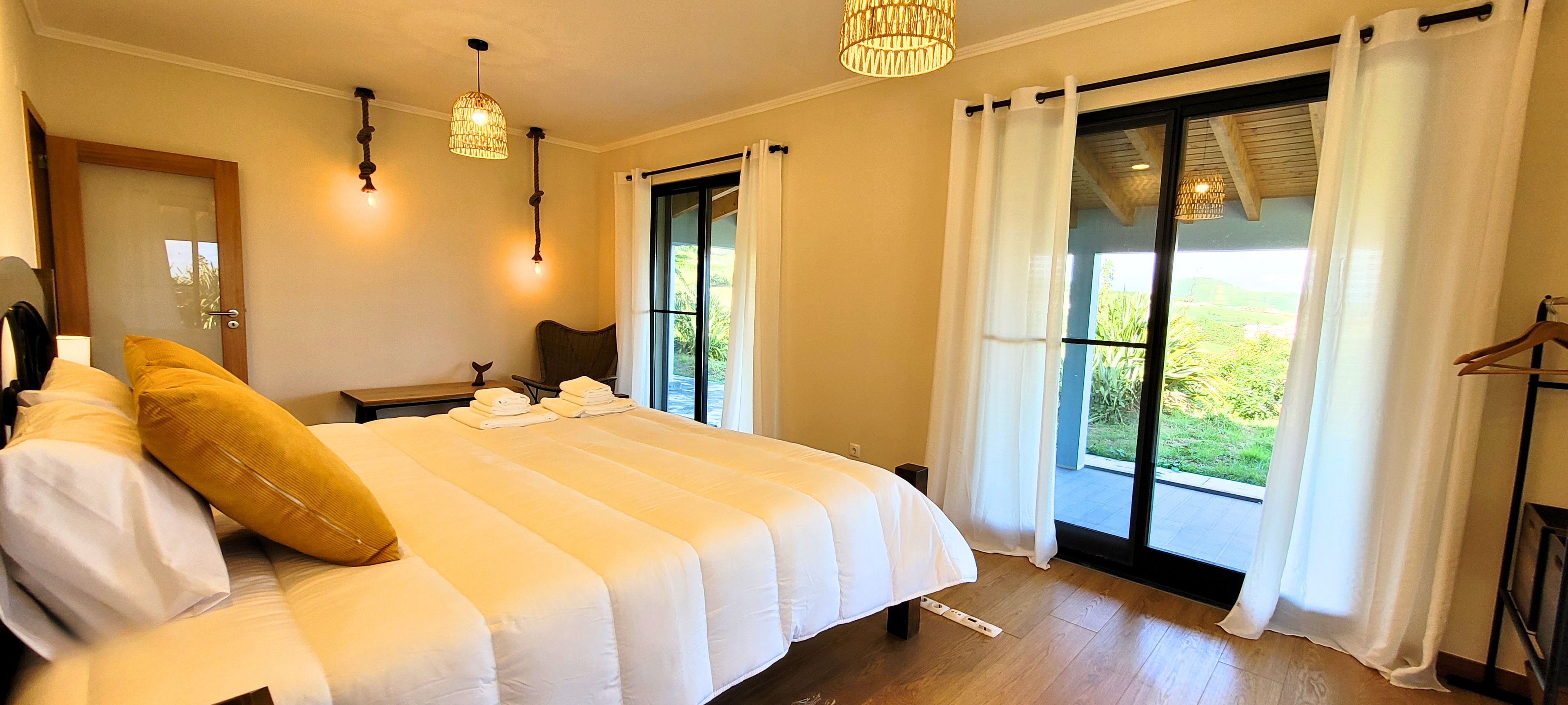 Een hotelkamer met een groot bed, twee nachtkastjes, een stoel en uitzicht door de ramen.