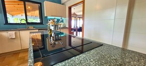 A modern kitchen with a black countertop, a wooden ceiling, and a view of a dining area.