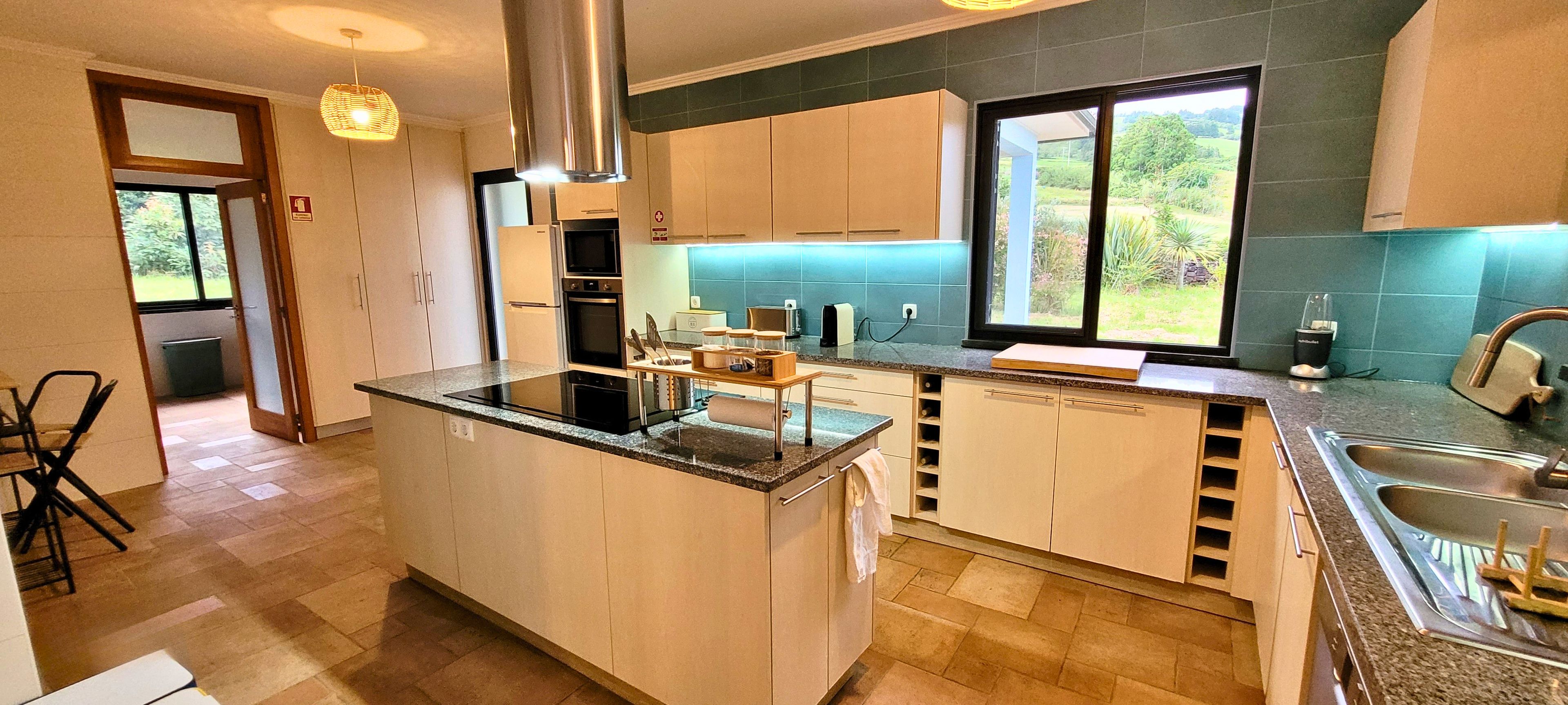A modern kitchen with a central island, stainless steel appliances, and a view of greenery outside.