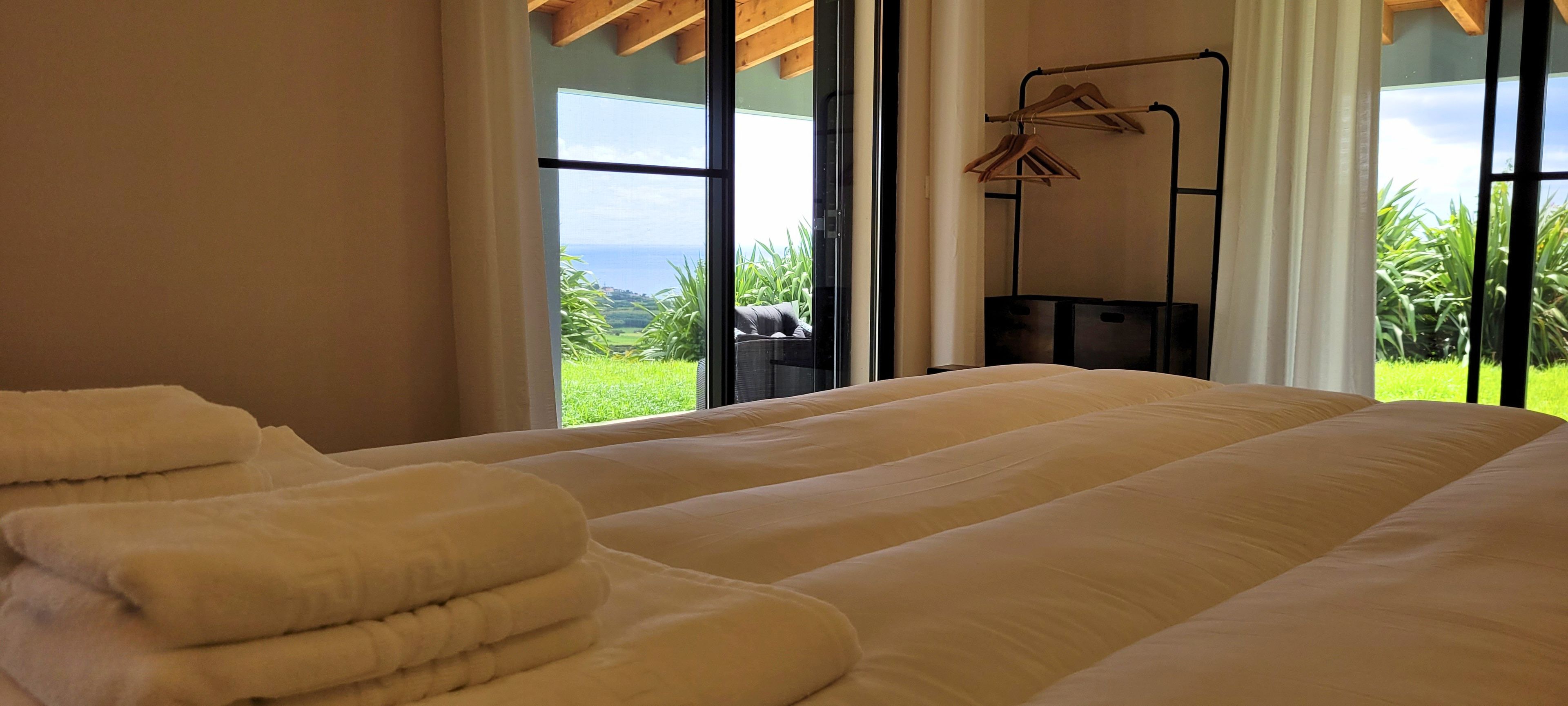 Habitación de hotel con una cama grande, una ventana con vistas a zonas verdes y al mar, y un tendedero con ropa.