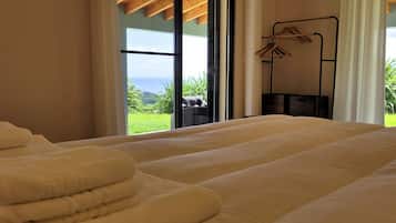 Habitación de hotel con una cama grande, una ventana con vistas a zonas verdes y al mar, y un tendedero con ropa.