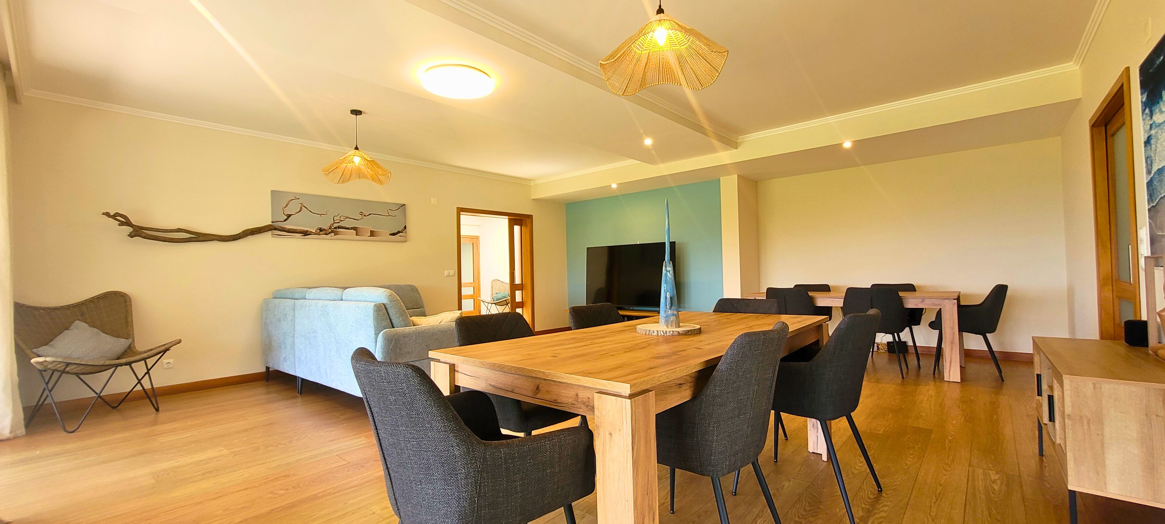 Uma sala de estar moderna com uma mesa de jantar de madeira, cadeiras pretas, um sofá e uma televisão.