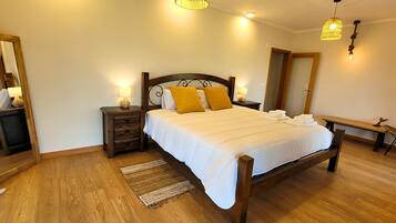 Een goed verlichte slaapkamer met een houten bed, nachtkastjes met lampen, een bankje en een stoel.