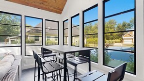 A sunlit room with large windows, a dining table, chairs, and a view of a swimming pool. - Private Pickleball Court - Year-Round Combo Pool and Hot Tub - Beach Access (South Haven)