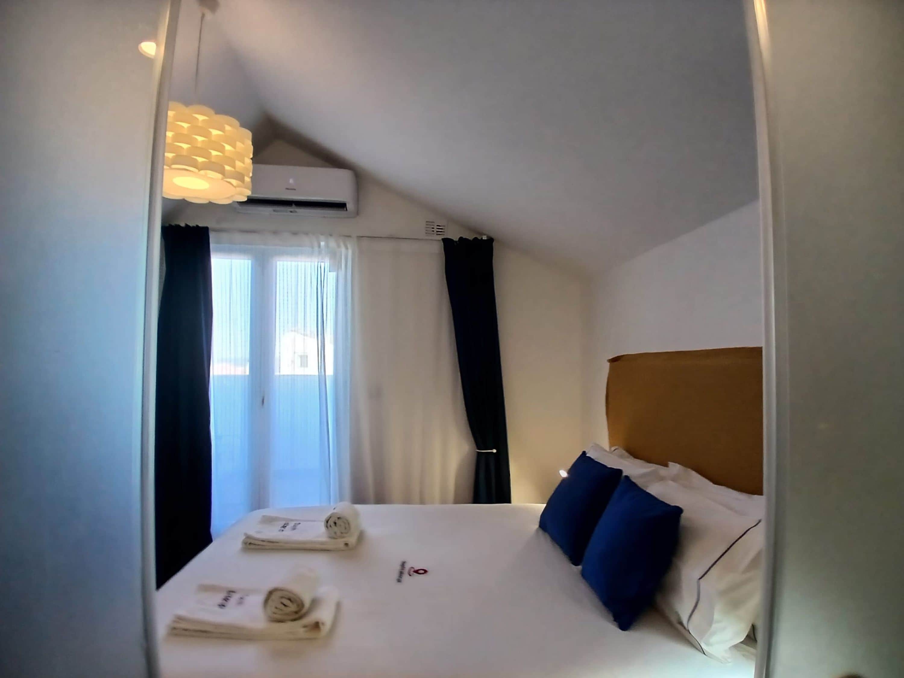 A hotel room with a bed, a ceiling fan, an air conditioning unit, and a window with curtains.