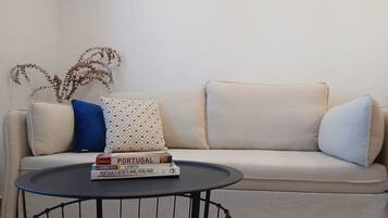 A beige sofa with patterned cushions, a small round table with books, and a decorative plant.
