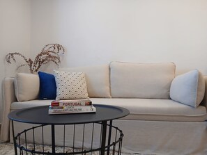 A beige sofa with patterned cushions, a small round table with books, and a decorative plant. - Blue House River View Balcony AC 2 En-suites (Lisbon)