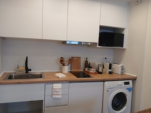 A compact kitchen with a microwave, toaster, and washing machine. - Blue House River View Balcony AC 2 En-suites (Lisbon)