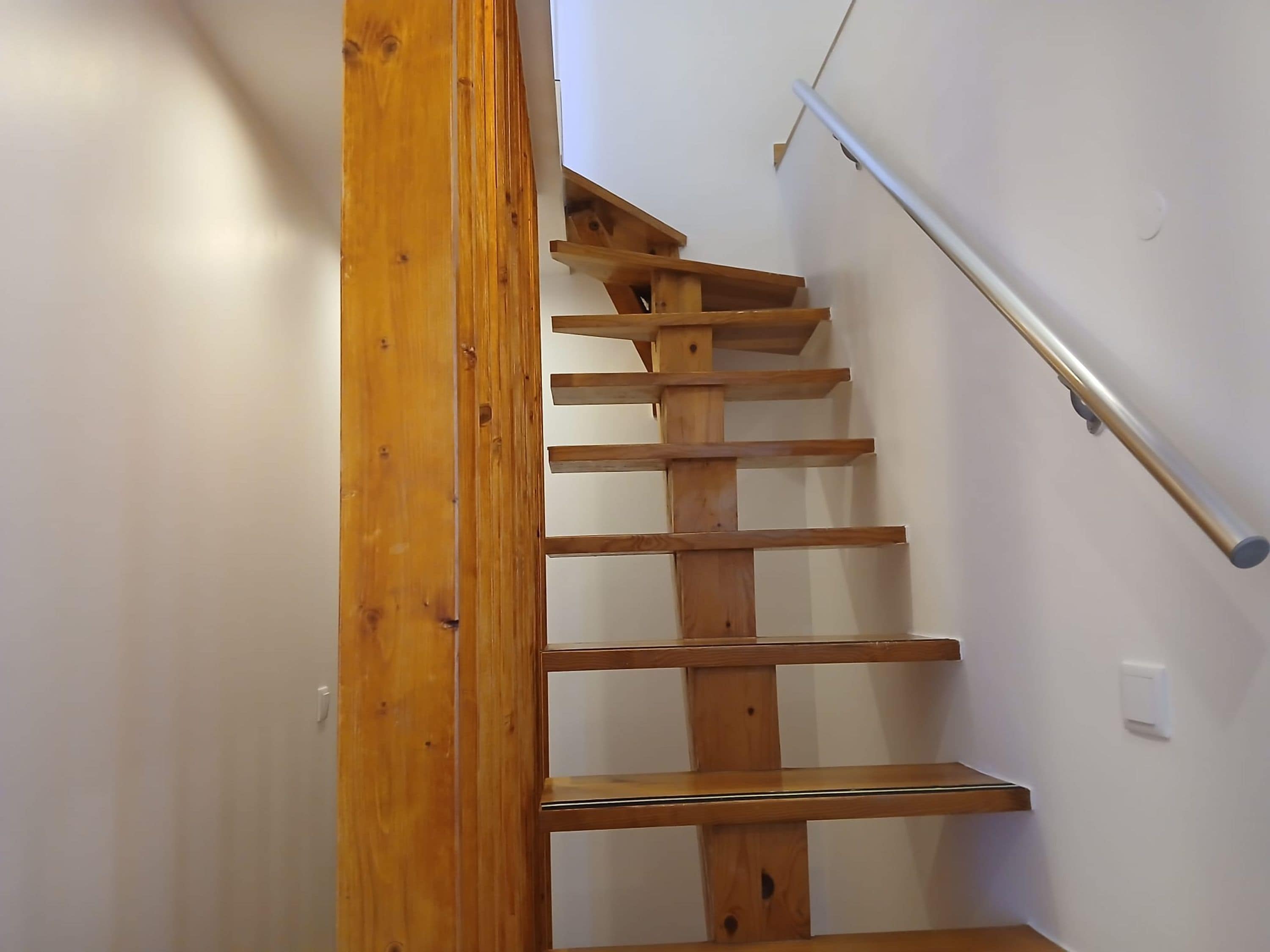 A wooden staircase with a handrail and a white wall.