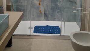 Ein modernes Badezimmer mit einer in Glas abgeschlossenen Dusche, einer blauen Fußmatte und einer großen Badewanne.