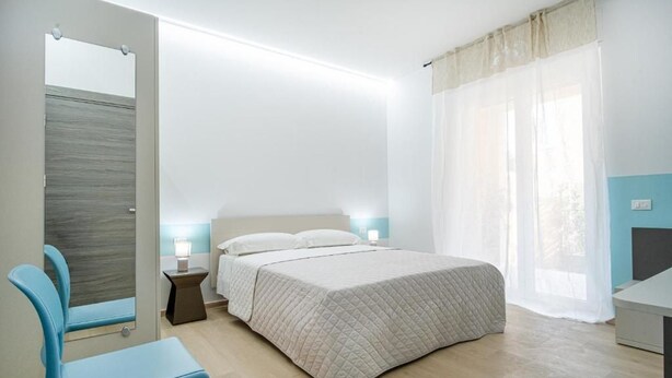 Ein Schlafzimmer mit einem Bett, einem Sessel, einem Nachttisch und einem Fenster mit Vorhängen.