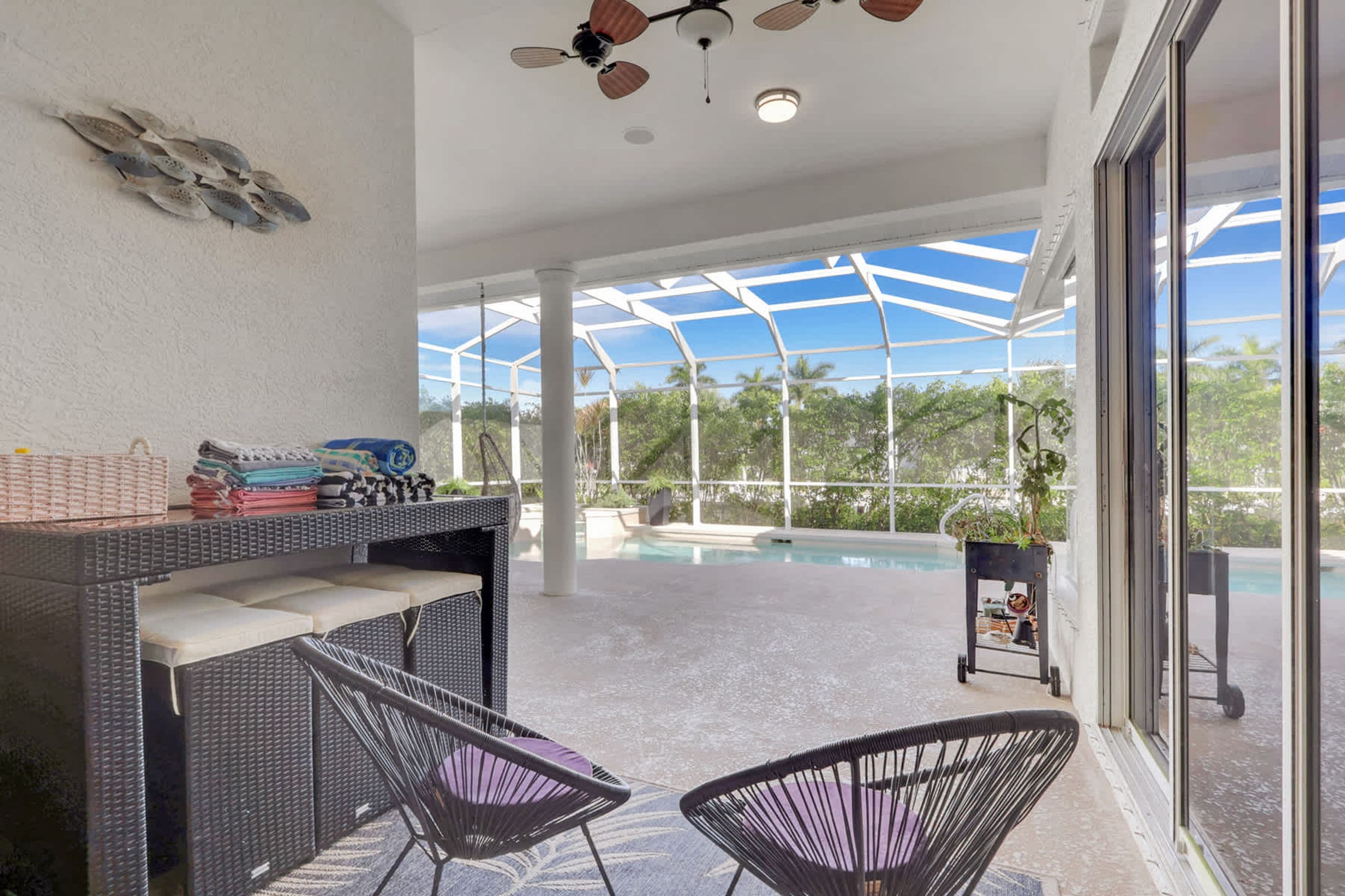 A covered outdoor area with a pool, wicker furniture, and a ceiling fan.