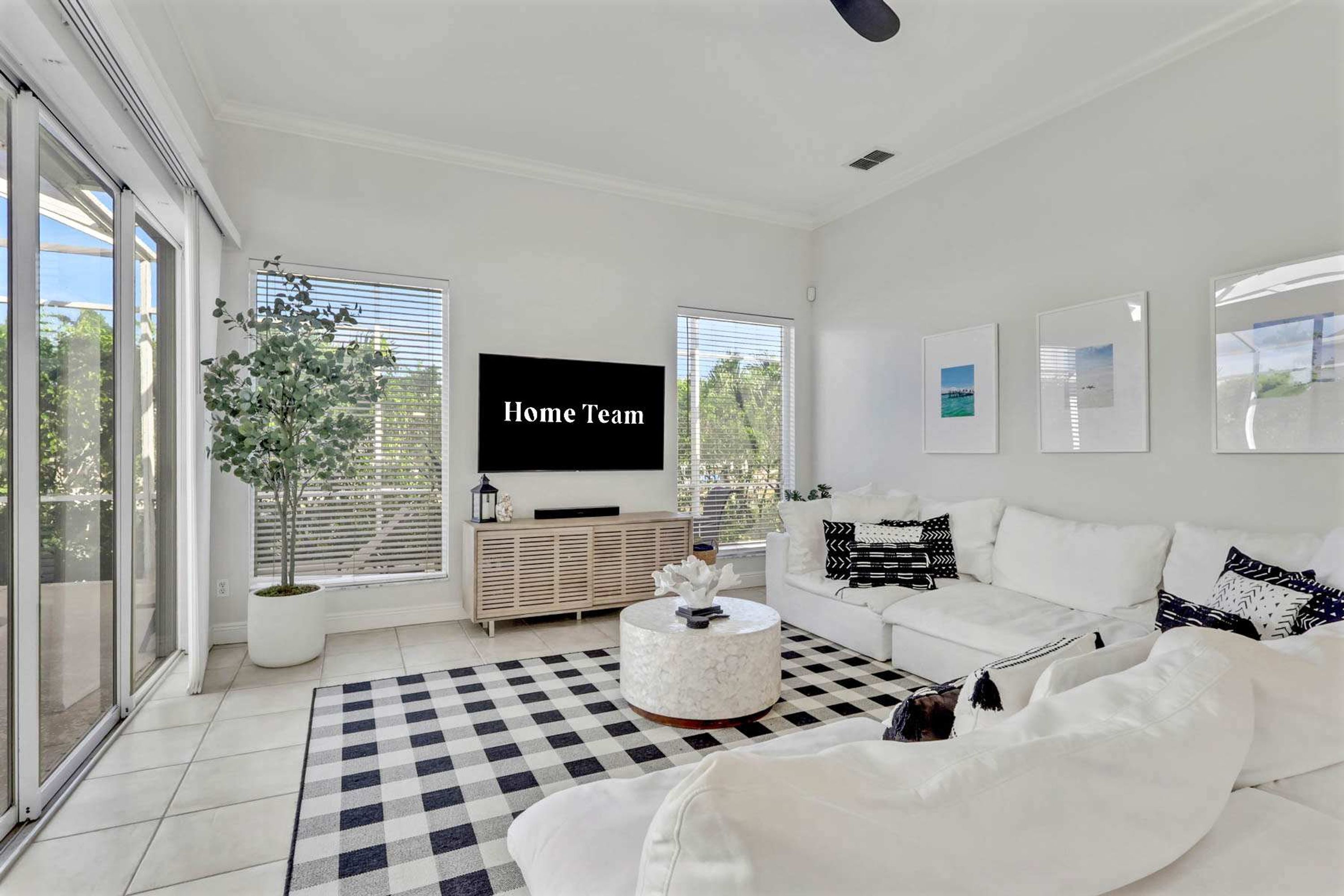A modern living room with a large flat-screen TV, a white sofa, a round coffee table, and a checkered rug.