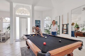 Ein Billardtisch in einem hellen Raum mit weißen Wänden und großen Fenstern.