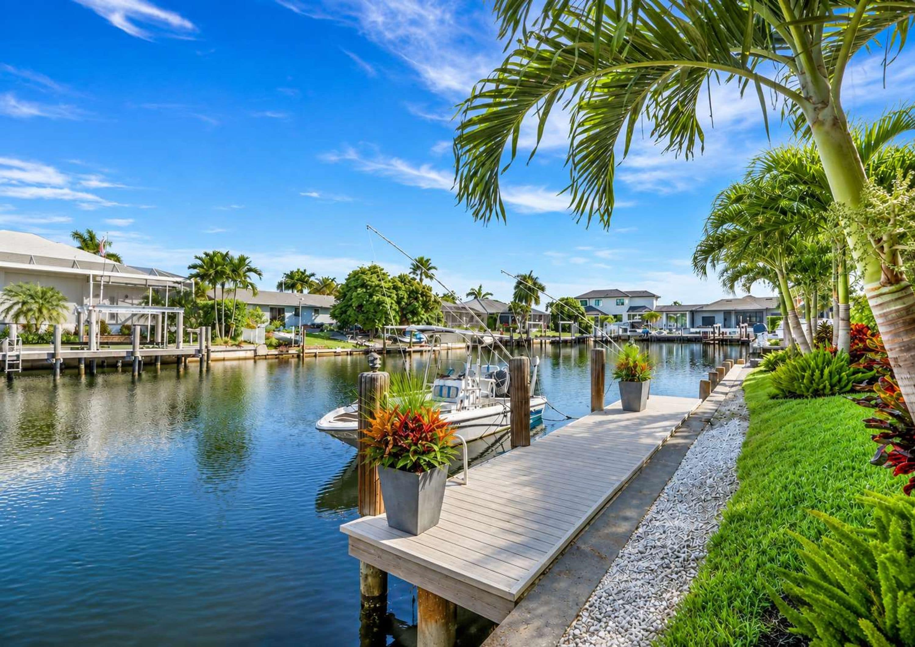 A marina with boats docked, a wooden dock, and a row of houses with a clear blue sky.