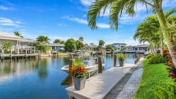 A marina with boats docked, a wooden dock, and a row of houses with a clear blue sky.