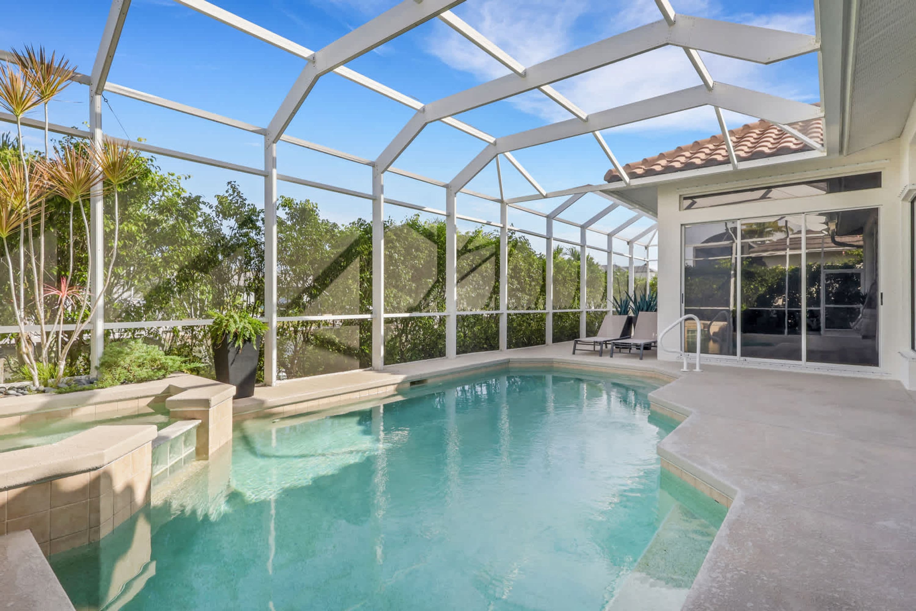 A swimming pool with a glass enclosure, surrounded by greenery and a clear sky.