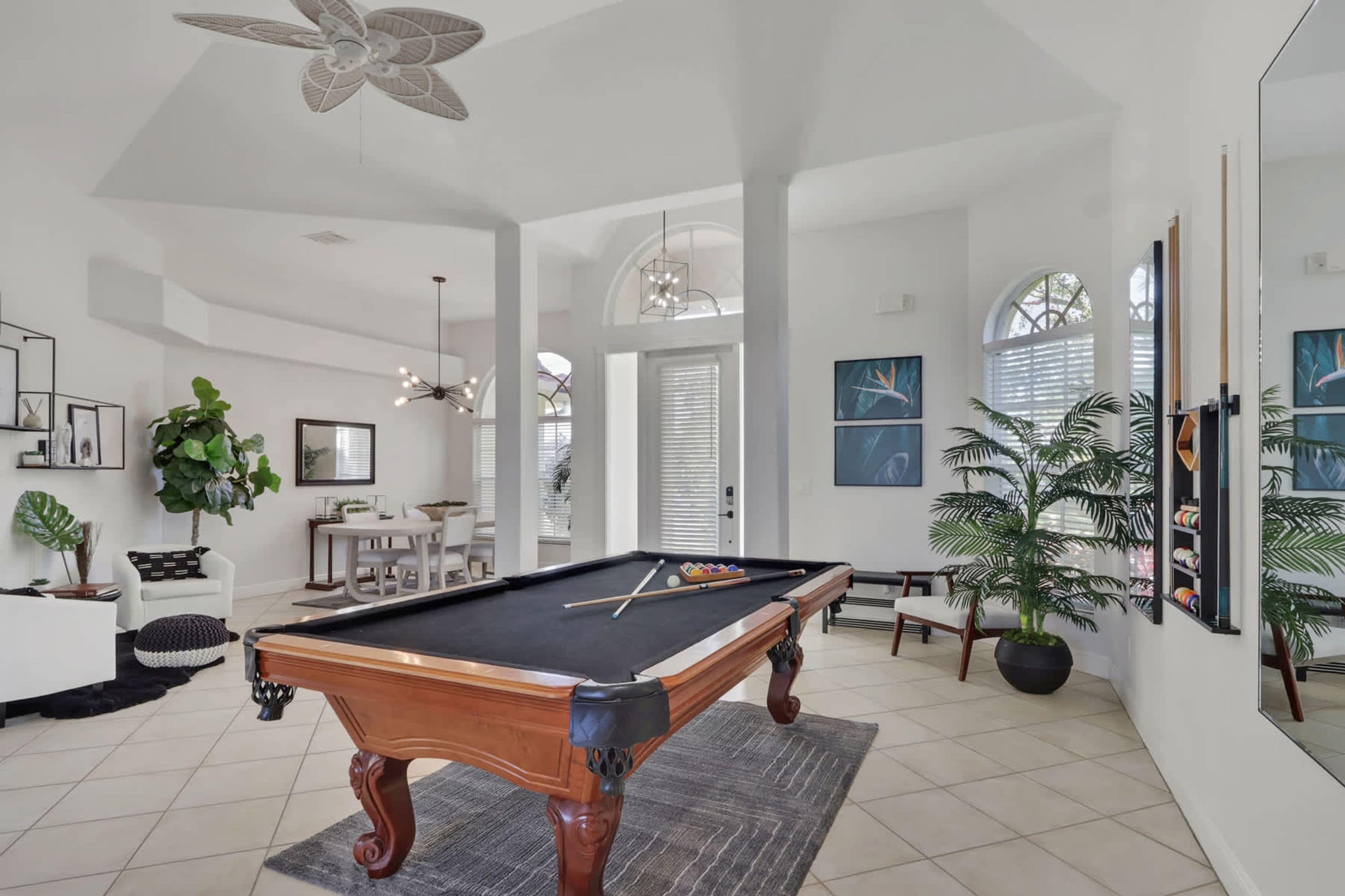 A spacious room with a pool table, a dining area, and a living space with large windows and ceiling fans.