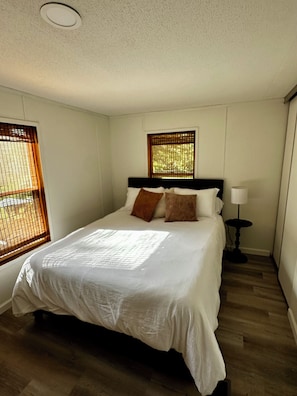 Ein Hotelzimmer mit einem großen Bett, einer Nachttischlampe und einem Fenster mit Jalousien.