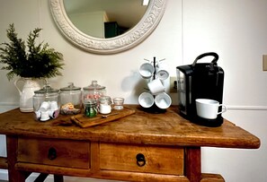 Un aparador de madera con espejo, una planta en maceta y varios utensilios de cocina, incluyendo frascos, una cafetera y tazas.