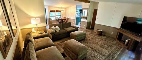 A living room with a sofa set, a television, and a dining area in the background.