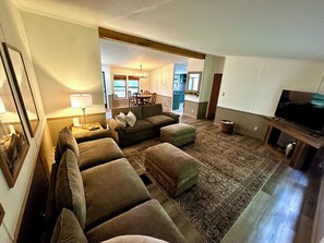 Una sala de estar con un conjunto de sofás, un televisor y un comedor al fondo.